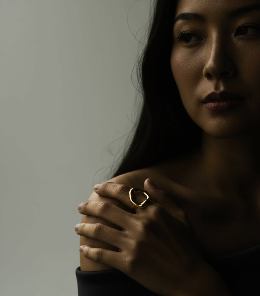 Woman wearing an 18k gold organic-shaped ring on a plain background